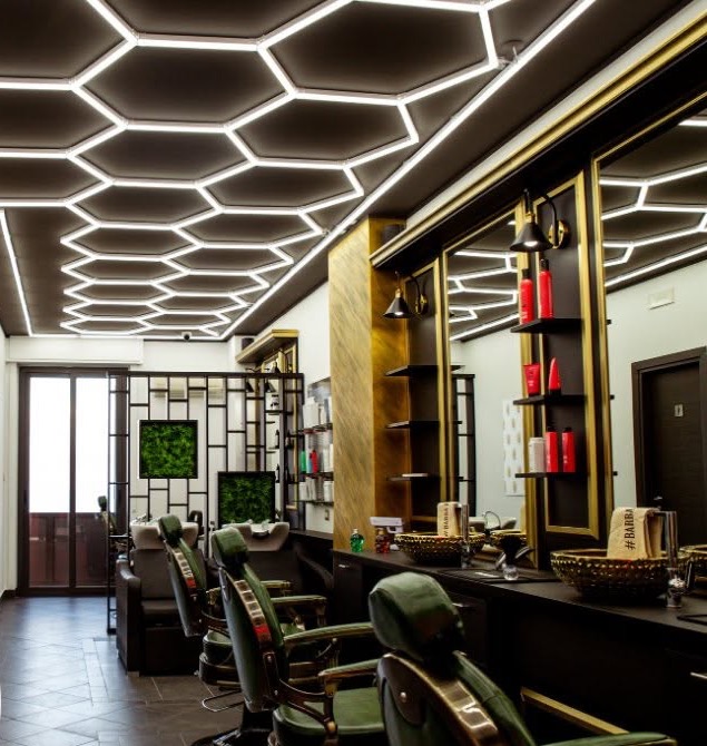 Il negozio: soffitto a esagoni di luce, poltrone da barbiere in pelle verde, specchi con cornici dorate