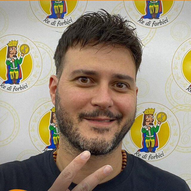 Ritratto di Antonio davanti alla parete coi loghi del negozio, sorridente