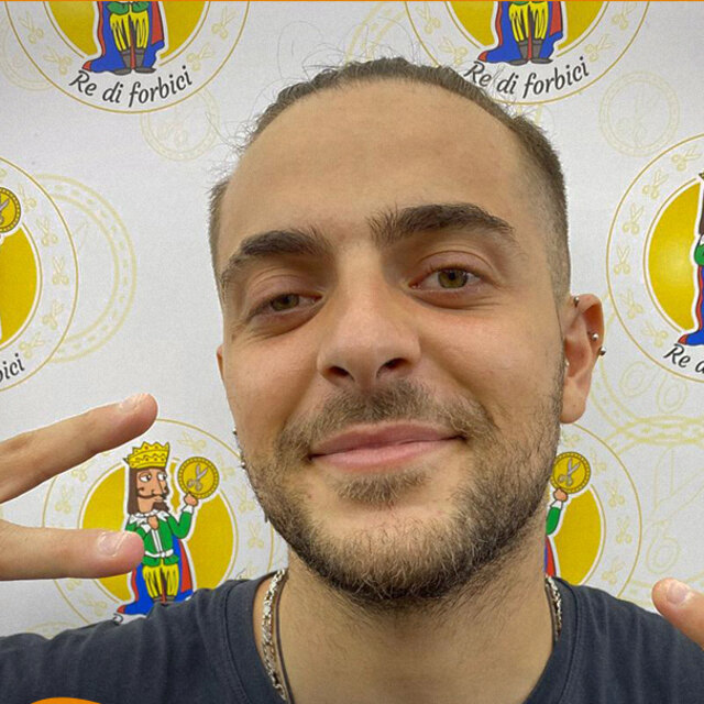 Ritratto di Davide davanti alla parete coi loghi del negozio, sorridente